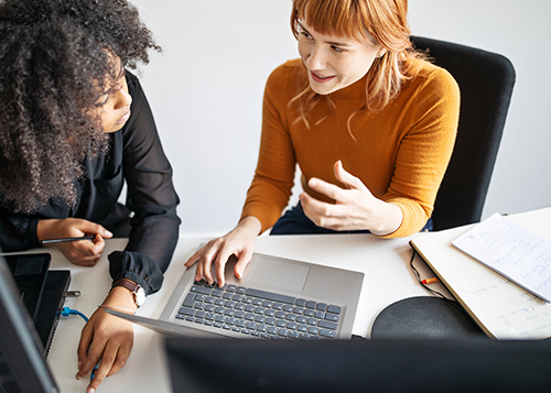 two women at a table talking in front of a computer