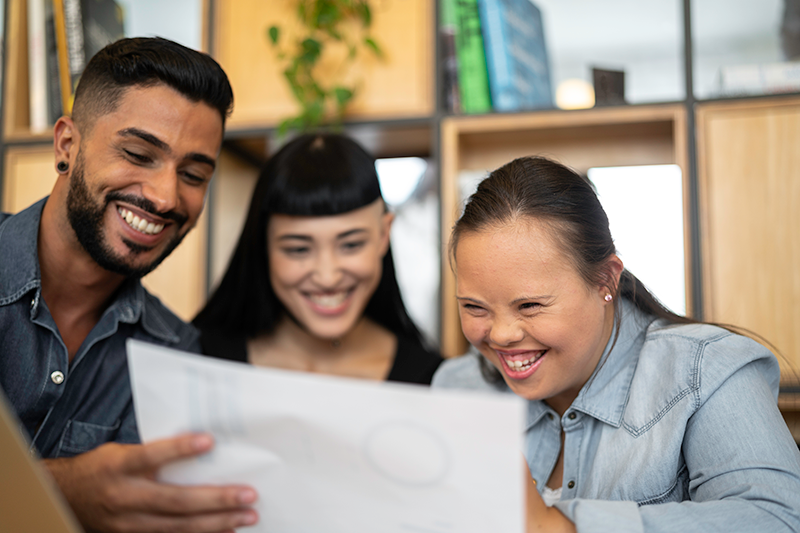 one man and two women smiling looking at paper