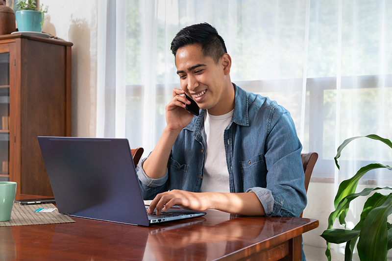 man looking at a laptop while talking on a cell phone