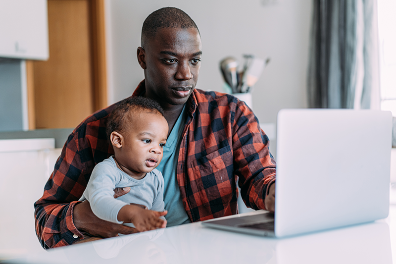 man sitting down holding baby looking at a laptop