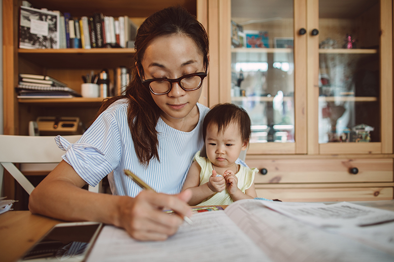 young woman at table writing holding a baby