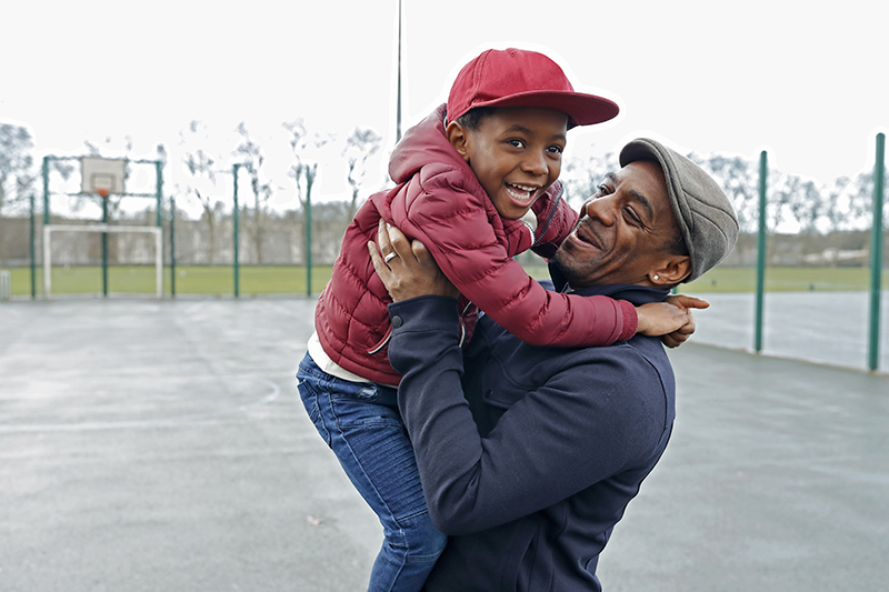 man picking up child both smiling at a basketball court