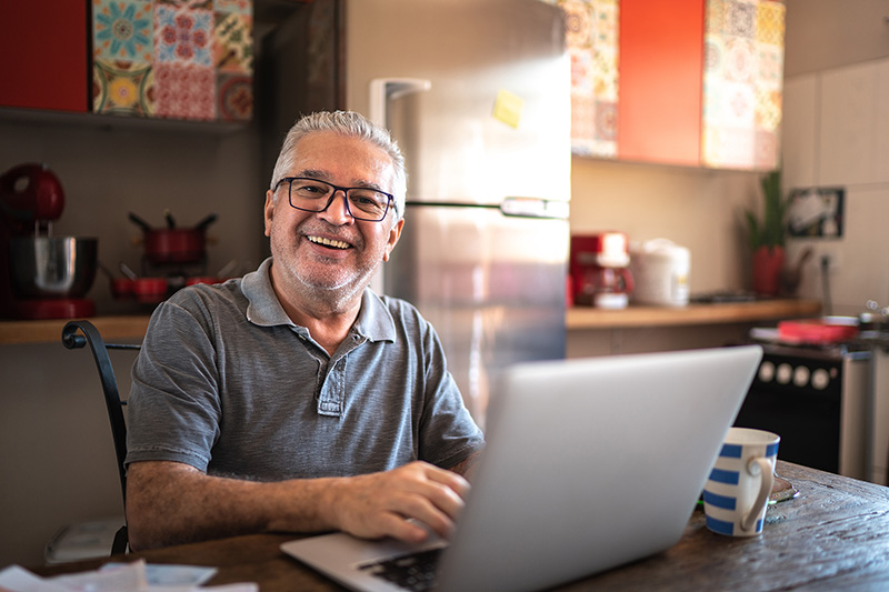older gentleman sitting at a table with laptop smiling