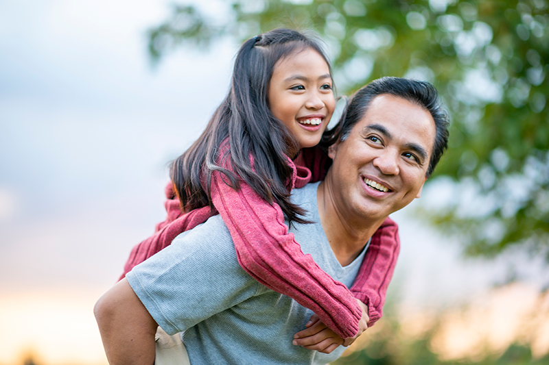 father carrying daughter on back outside