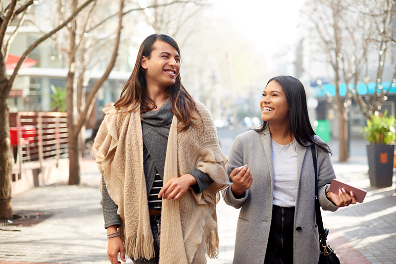 two people walking down the street laughing and talking