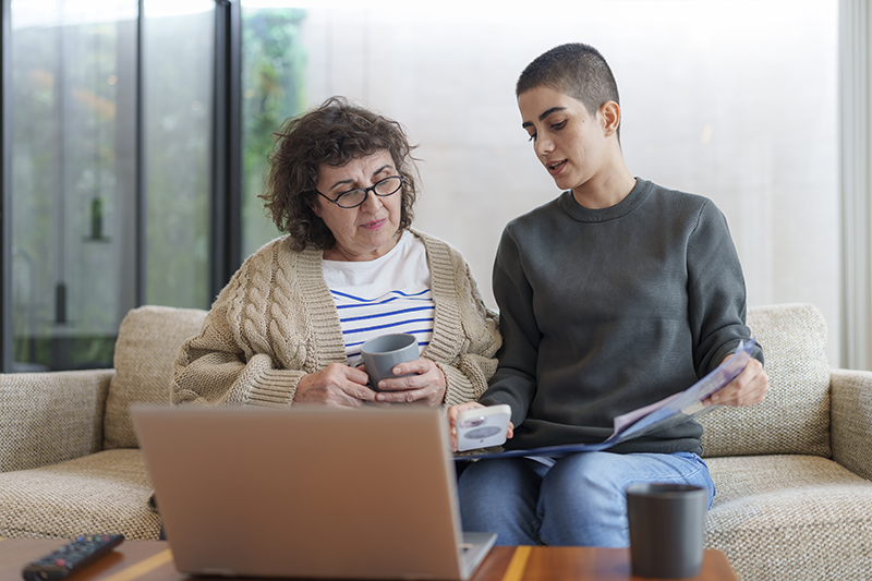 two people talking while looking at papers in front of a computer