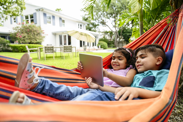 two kids in a hammock looking at a tablet