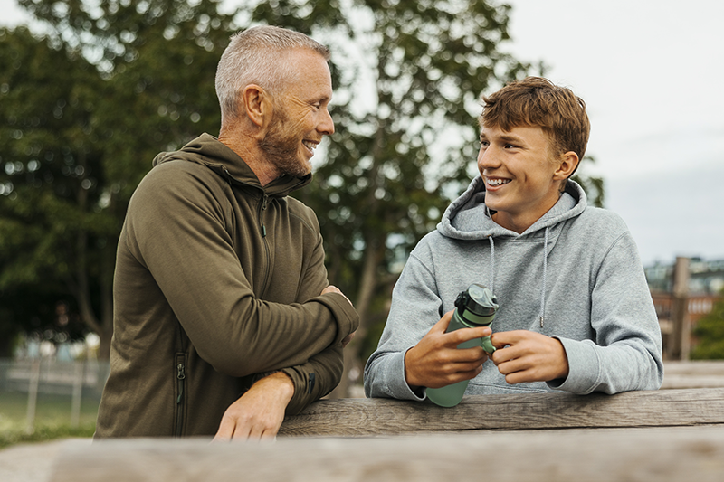 man and teenage boy outside looking at each other and smiling